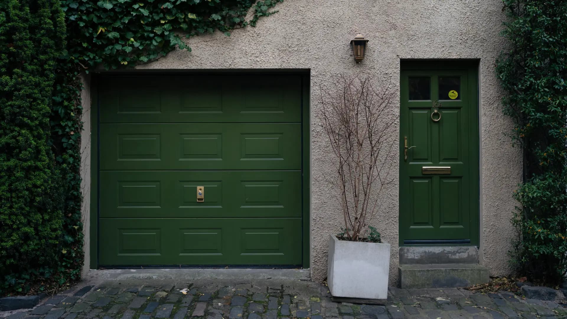Porte de garage à cassettes et porte d'entrée vert foncé sur une façade en crépi